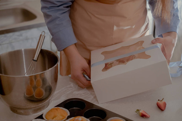 Una chef de pastelería empaca cupcakes en envases para enviar a los clientes, mostrando hornear en casa. Experimente la esencia de hornear a pequeña escala y respetuoso del medio ambiente con productos sin gluten y sin azúcar, promoviendo una alimentación saludable. - Foto, imagen