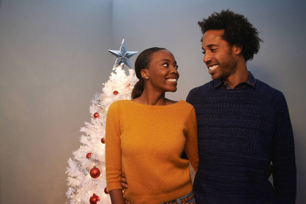 Kerstmis, boom en zwart paar met liefde in huis op vakantie of knuffel op vakantie met geluk. Feestelijk, huis en mensen omarmen met zorg en steun of opgewonden om samen op het evenement te vieren. - Foto, afbeelding