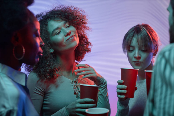 Талия портрет красивых молодых девушек, танцующих на домашней вечеринке и держащих красные чашки с алкоголем - Фото, изображение