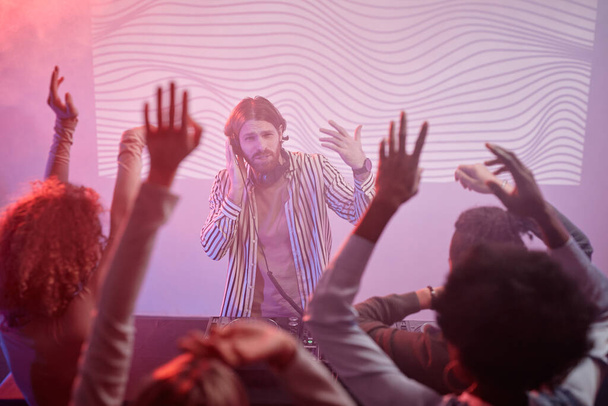 Portrét DJ u otočného stolu v neonových světlech, jásající nad tanečním davem na diskotéce - Fotografie, Obrázek