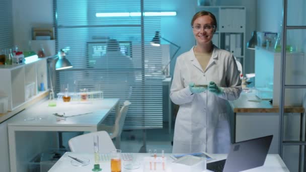 Retrato lento médio de jovem cientista branca sorrindo para a câmera em pé no laboratório moderno com musgo verde na placa de Petri nas mãos - Filmagem, Vídeo