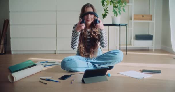 自宅でヘッドフォンを通して音楽を聴く床に横足に座っている若い女性ブルネットの全長 - 映像、動画