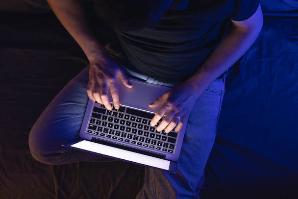 Gece geç saatlerde dizüstü bilgisayar başında meşgul bir adam, mesaj yazıyor, fazla mesai yapıyor, internette sörf yapıyor. Aşırı çalışma ve uzaktan çalışma konsepti. Karanlık odada sergilenen ışıktan. - Fotoğraf, Görsel