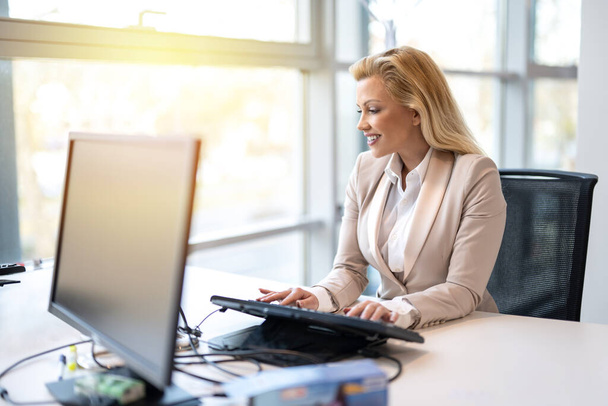 Piękne blond włosy kobieta w biznesie formalny strój pracy na komputerze w biurze. - Zdjęcie, obraz