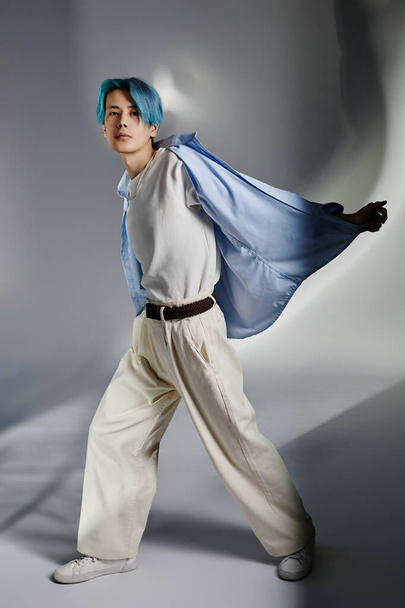 Vertical image of young dancer with blue hair and in stylish clothing exercising on grey background - Foto, Bild