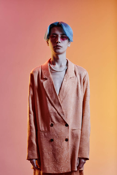 Vertical image of Asian young guy with blue hair and in stylish jacket looking at camera standing against colored background - Foto, Imagem