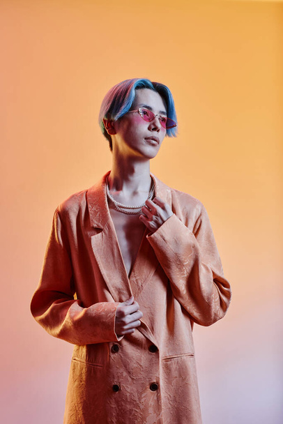 Vertical image of stylish guy with blue hairstyle and trendy jacket standing against colored background - 写真・画像