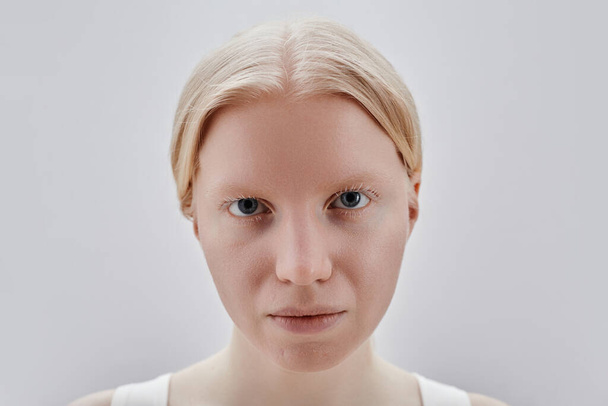 Closeup portrait of blonde girl looking at camera with intense face expression against white background - Photo, Image