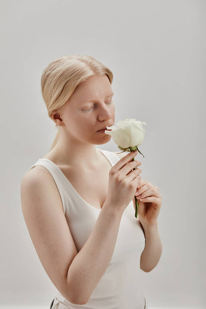 Мінімальний вертикальний портрет красивої молодої жінки з альбінізмом, що тримає білу троянду - Фото, зображення