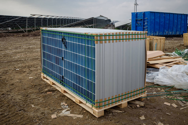 太陽光発電所の建設現場でソーラーモジュールと太陽光パネルのコンポーネントを含むパレット. バックグラウンドでの設置および建設廃棄物のためのパレットに積み重ねられたソーラーパネル. - 写真・画像