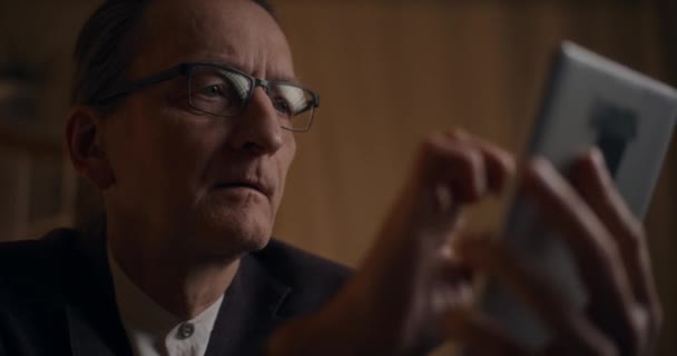 Seriöser Geschäftsmann mit Brille liest spätabends am Arbeitsplatz auf digitalem Tablet - Filmmaterial, Video