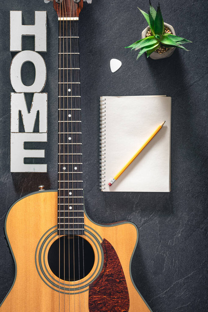 Ακουστική κιθάρα, σημειωματάριο και διακοσμητική λέξη Home, top view. Δημιουργικό μουσικό υπόβαθρο. - Φωτογραφία, εικόνα