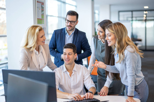 Grupa odnoszących sukcesy pracowników firmy współpracujących ze sobą i mających spotkanie w pobliżu komputera w nowoczesnym biurze. - Zdjęcie, obraz