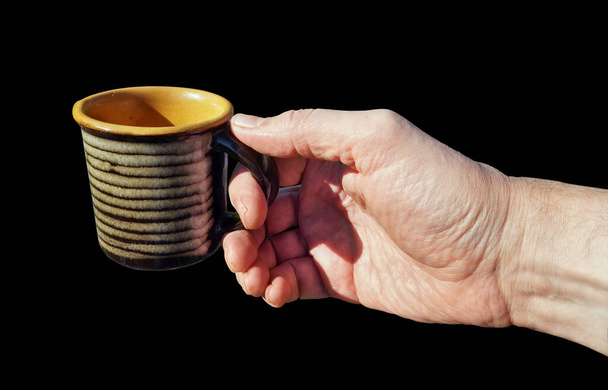 Um homem tem uma caneca de cerâmica vazia na mão. Isolado em preto - Foto, Imagem