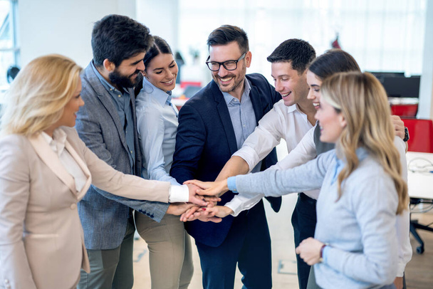 Groep zakenmensen stapelen handen in een krappe cirkel, om hun eenheid in het kantoor te strategiseren, te motiveren of te vieren. - Foto, afbeelding