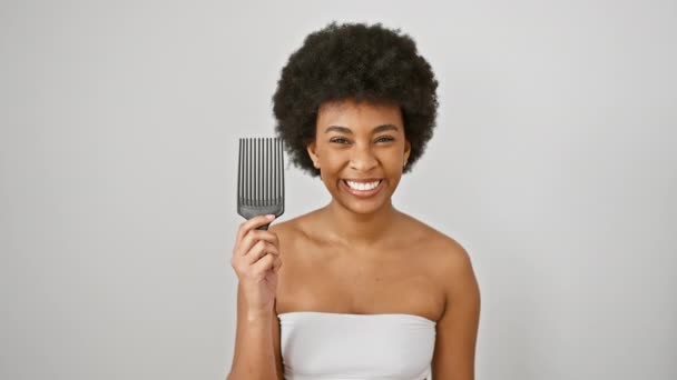Astonished african american woman with comb, expresses shock and disbelief, mouth open in amazed wonder on isolated white background     - Footage, Video