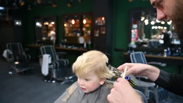 Borbély fésűt és borotvát használ a hajvágáshoz. Professzionális fodrász borotválkozás kisgyerekek alvás. - Felvétel, videó