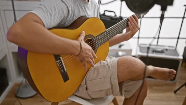 Vousatý muž hrající na akustickou kytaru, se zaměřením na akordy ve sluncem osvětleném nahrávacím studiu. - Záběry, video