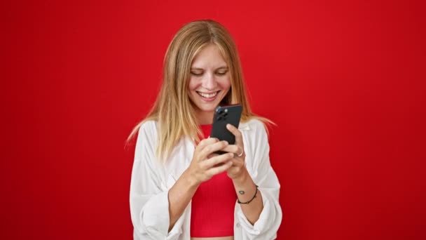 Hymyilevä nuori nainen käyttää älypuhelinta punaista taustaa vasten - Materiaali, video