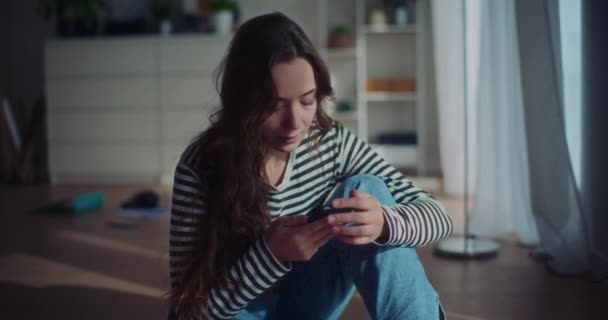 Zeitlupenaufnahme einer einsamen Frau mit Smartphone, die zu Hause im Wohnzimmer auf dem Boden sitzt - Filmmaterial, Video