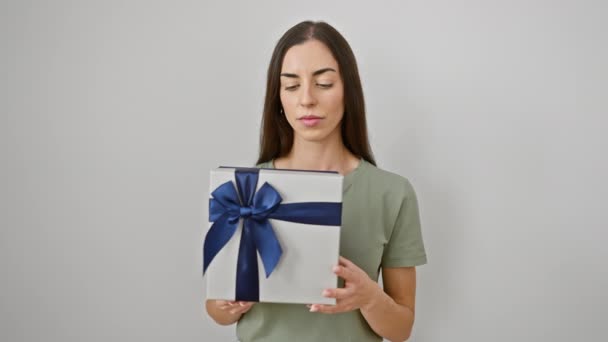 Αυτοπεποίθηση νεαρή ισπανόφωνη γυναίκα, φαίνεται σοβαρή, σκέπτεται με πακέτο δώρων, στέκεται απέναντι σε απομονωμένο λευκό φόντο - Πλάνα, βίντεο