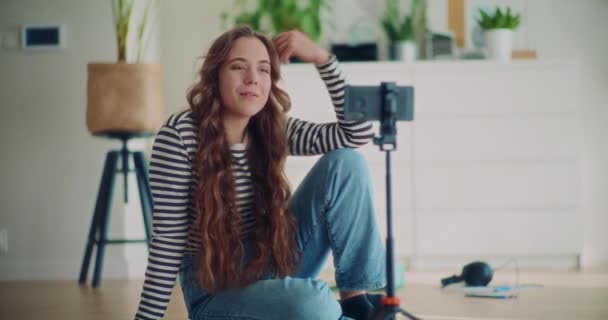 Mooie jonge vrouwelijke content maker filmen zichzelf praten in de voorkant van de smartphone op statief thuis - Video
