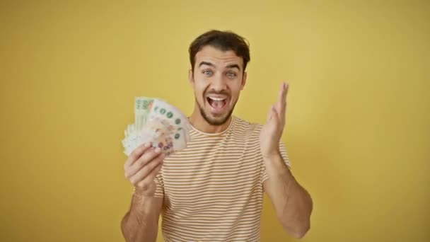 Victorious young hispanic man, gleefully holding money, celebrates with a joyous winner smile, expression of triumphant happiness. isolated on a vibrant yellow background, cheers his win. - Footage, Video