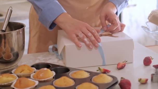 Een vrouwelijke banketbakker die cupcakes in een doos verpakt. Thuis bakken, kleine bedrijven, milieuvriendelijke productie, glutenvrij, suikervrij, bevorderen van gezonde eetgewoonten. - Video