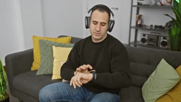 男はヘッドフォンで音楽を聴き,装飾的な枕付きの居心地の良いソファーで自宅でリズムを感じる. - 映像、動画