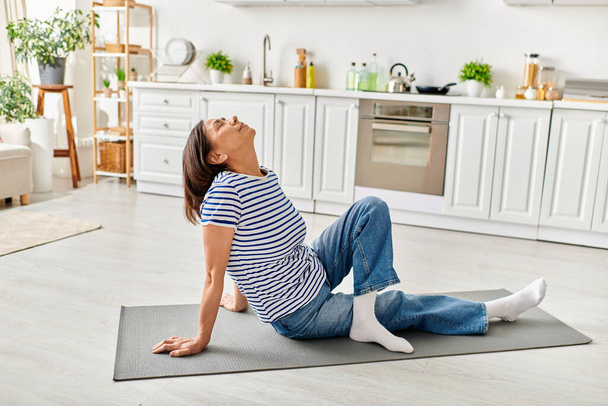 Una donna matura in accoglienti pratiche di usura yoga su un tappeto da cucina. - Foto, immagini