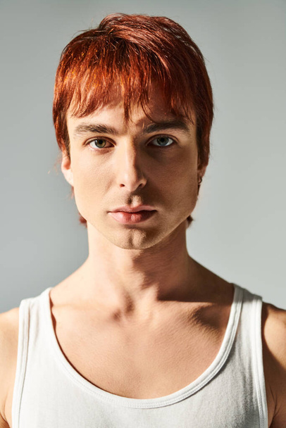 Tyylikäs nuori mies punaiset hiukset iskee poseeraa toppi vastaan harmaa studio tausta. - Valokuva, kuva