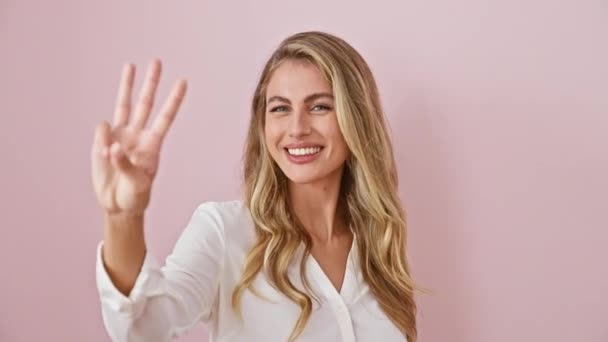 Radosna młoda blondynka ubrana w koszulę, wskazująca trzy palce uśmiechem na twarzy, sygnalizująca numer trzy szczęśliwej koncepcji na odosobnionym różowym tle. - Materiał filmowy, wideo