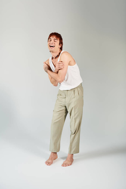 Un jeune homme élégant dans un débardeur blanc et pantalon kaki frappe une pose dans un cadre de studio avec un fond gris. - Photo, image