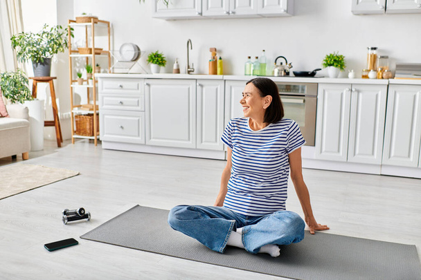 Reife Frau in gemütlicher Hauskleidung praktiziert Yoga auf einer Matte in ihrem Wohnzimmer. - Foto, Bild