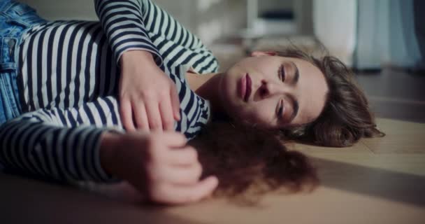 孤独な若い女性ブルネットのロックダウンショット自宅のリビングルームで日光の下で床でリラックス - 映像、動画
