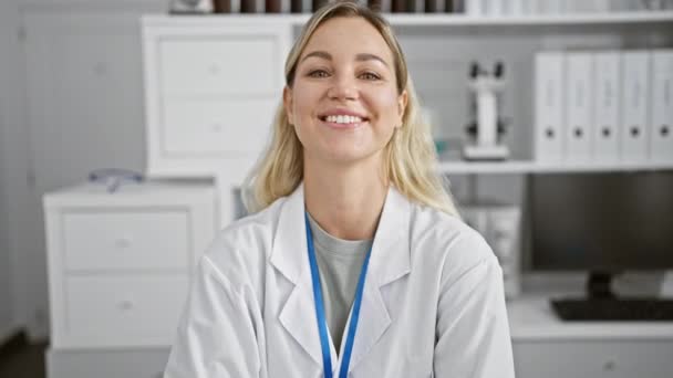 Una giovane donna sorridente in un camice da laboratorio con un cordino si trova in un laboratorio con armadi e attrezzature sullo sfondo. - Filmati, video