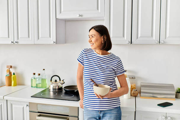 Érett nő kényelmes otthoni ruházat kezében egy tál a konyhában. - Fotó, kép