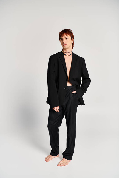 Ein stilvoller junger Mann im schwarzen Anzug steht selbstbewusst vor einem schlichten weißen Hintergrund in einem Studio-Setting.. - Foto, Bild