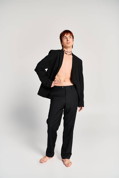 Un joven con estilo en un traje da una pose confiada contra un fondo gris de estudio. - Foto, Imagen