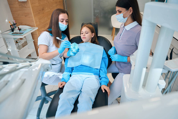 Meisje bij een afspraak met een arts hygiënist, een vrouw leert een patiënt hoe ze haar tanden correct moet poetsen - Foto, afbeelding