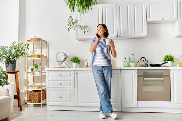 Зріла жінка в затишному домашньому вбранні насолоджується миттю на своїй кухні, тримаючи чашку. - Фото, зображення