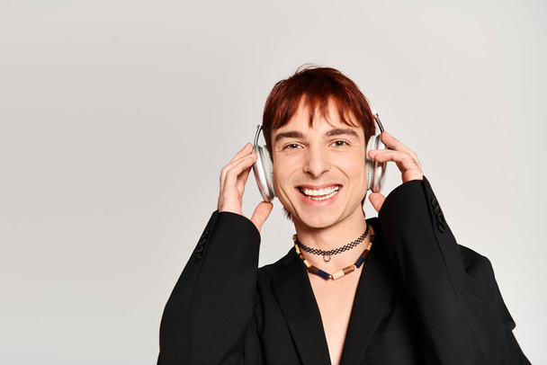 Een stijlvolle jongeman met rood haar in een koptelefoon tegen een grijze studio achtergrond. - Foto, afbeelding