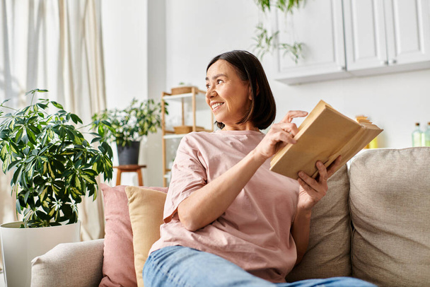 Kypsä nainen homewear lukee kirjan mukavasti sohvalla kotona. - Valokuva, kuva