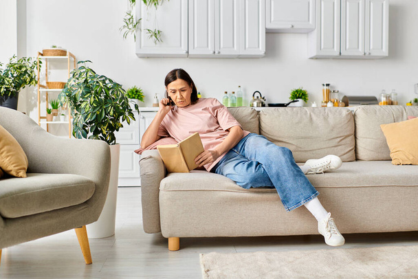 Kobieta w przytulnym homewear siedzi na kanapie, pochłonięta książką do czytania. - Zdjęcie, obraz