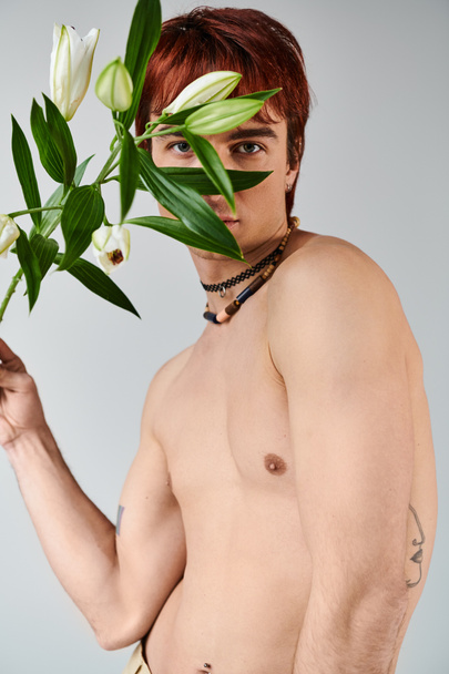 A young man with no shirt is holding a bunch of flowers against a grey background in a studio setting. - Photo, Image