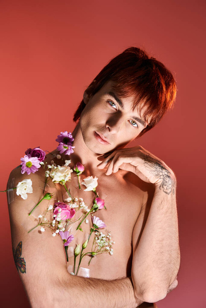 Un giovane senza maglietta si trova in uno studio, con fiducia in mano un mazzo di fiori vibranti sullo sfondo. - Foto, immagini