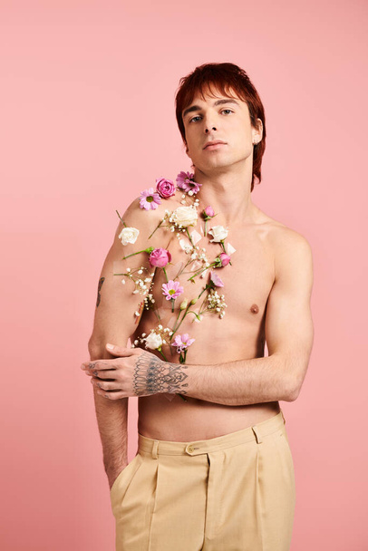 Un jeune homme torse nu tient avec confiance un beau bouquet de fleurs dans un élégant studio rose. - Photo, image