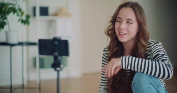 Привлекательная молодая брюнетка влиятельный делает vlogging через мобильный телефон в гостиной на дому - Кадры, видео