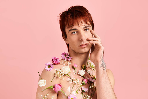 Un jeune homme aux cheveux roux saisissants pose avec confiance dans une chemise florale colorée sur un fond rose neutre. - Photo, image