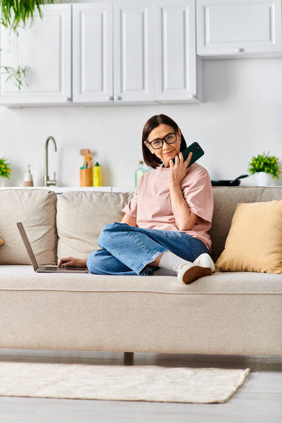 Žena v útulných domácích šatech sedí na gauči a vede telefonickou konverzaci.. - Fotografie, Obrázek